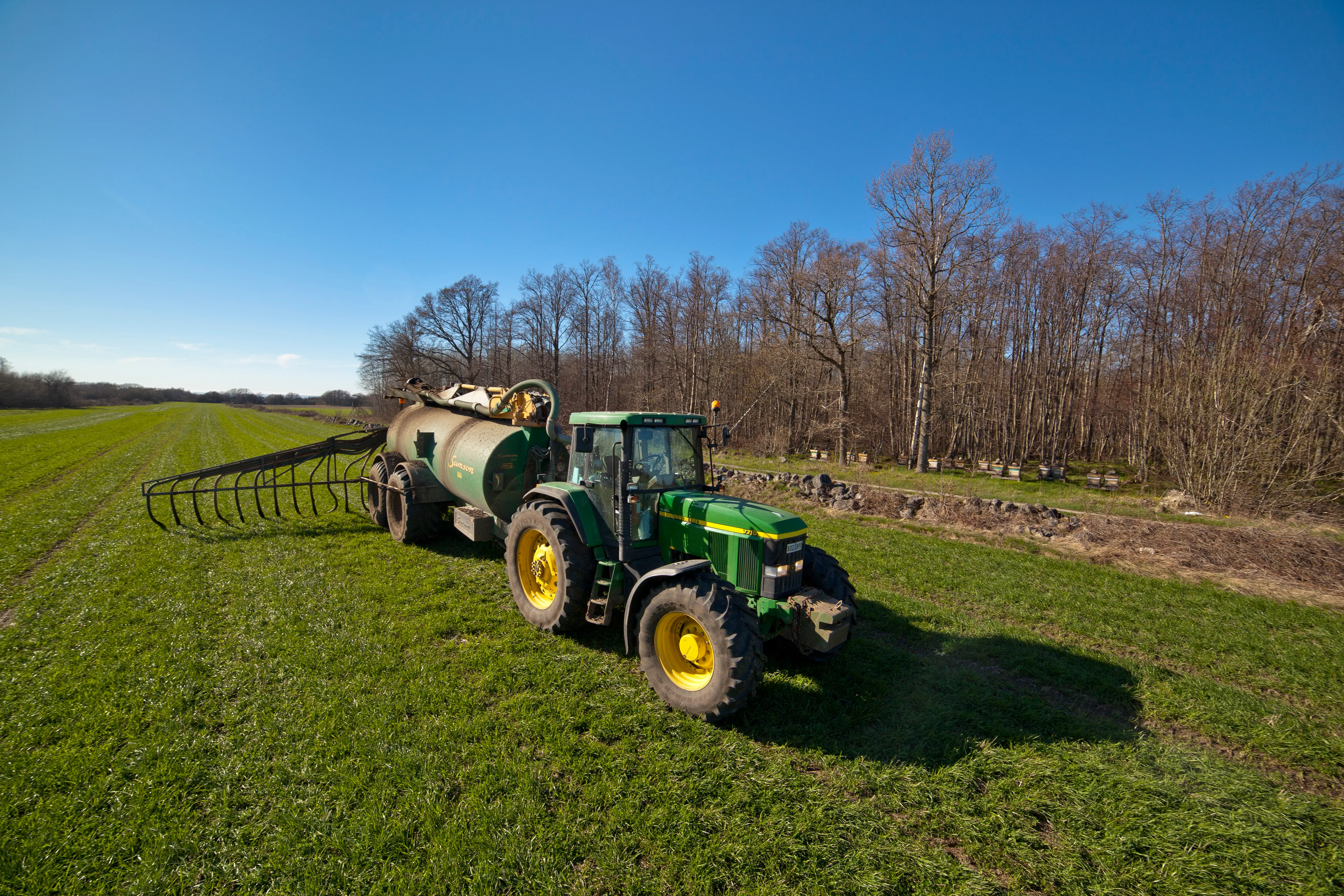 Traktor som sprider gödsel i vall med en svämtunna med släpslangar