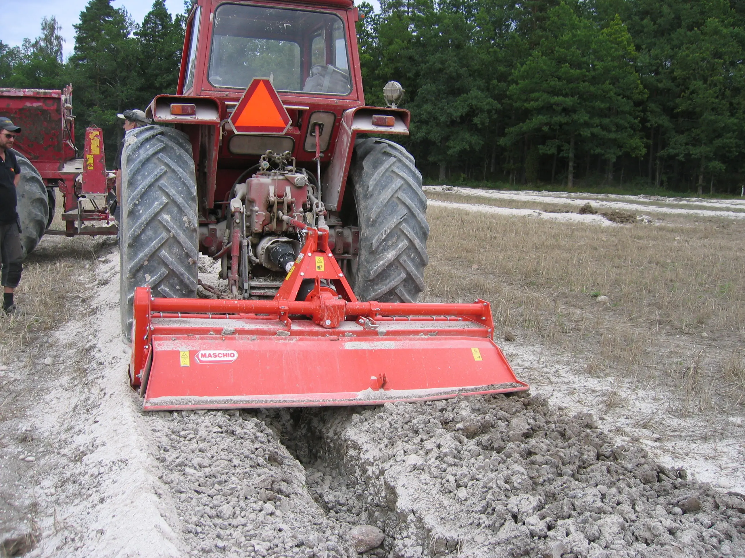 Traktor som fyller igen ett schakt efter täckdikning med kedjegrävare.