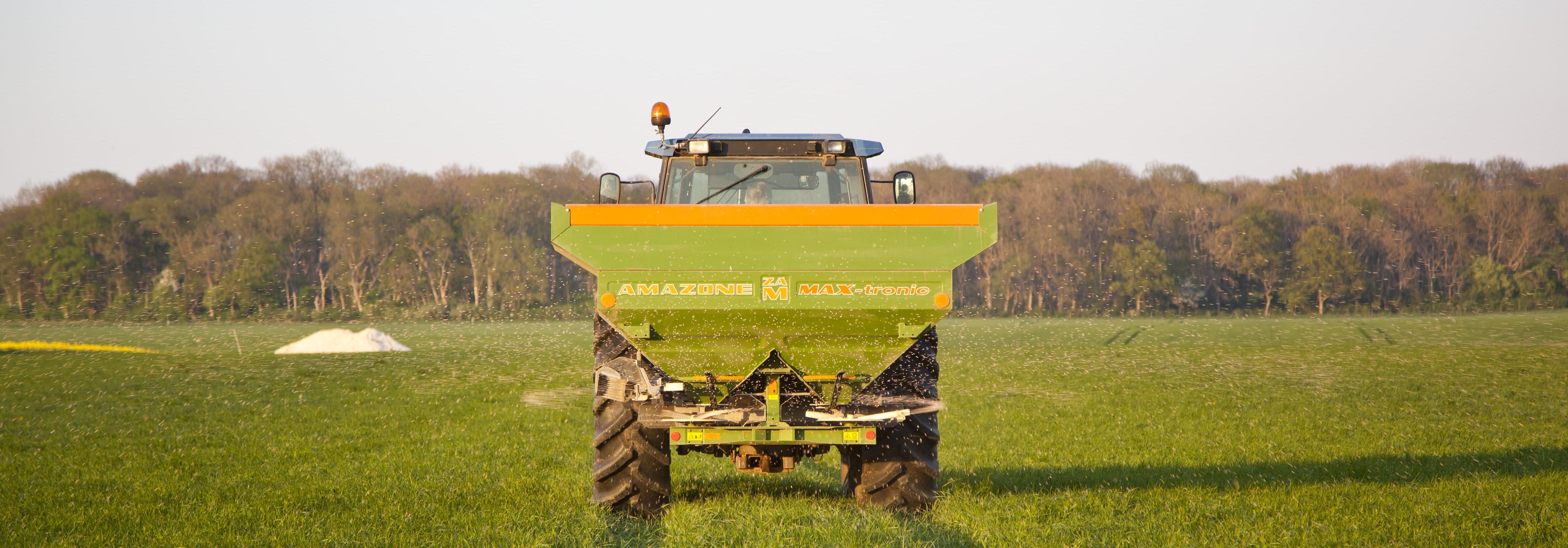 Traktor som sprider handelsgödsel med en slunga i vall