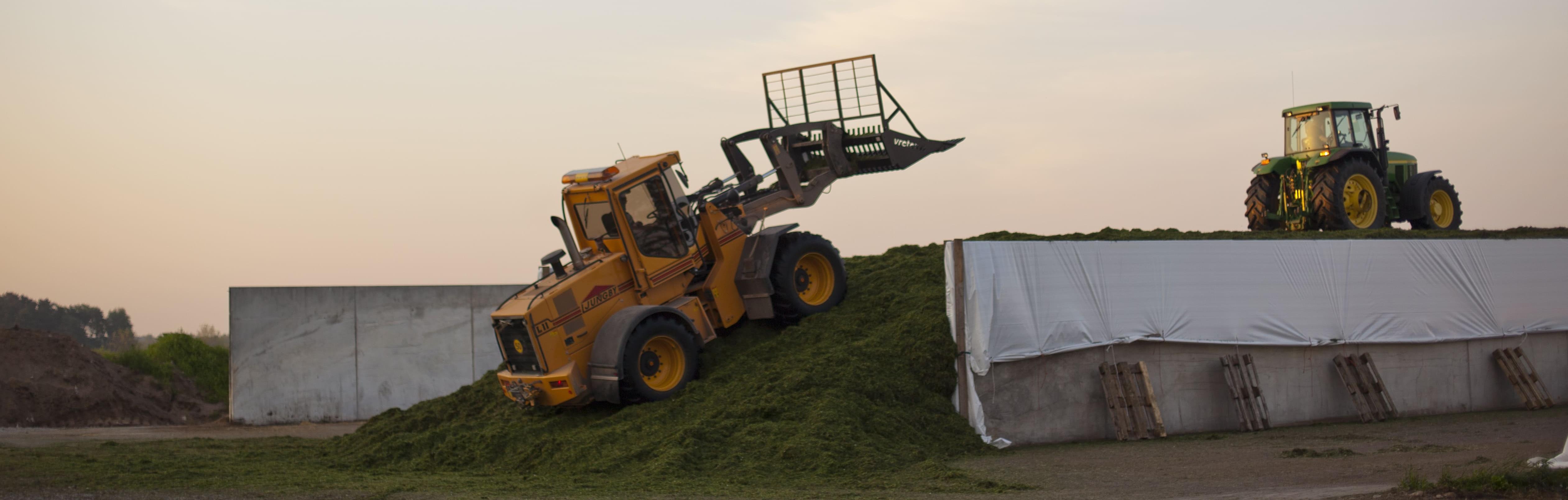 Traktor och lastmaskin packar gräs i en plansilo