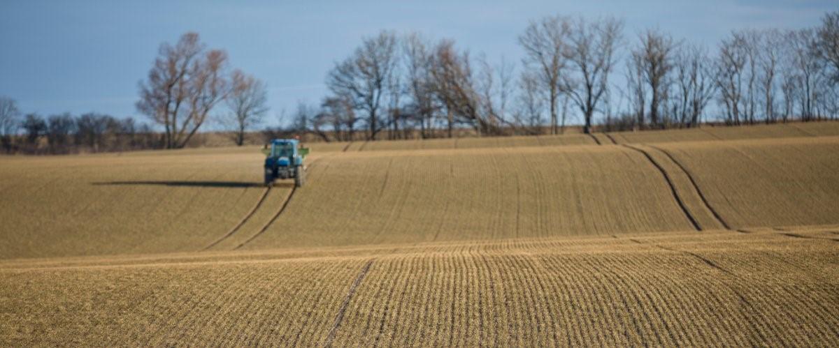 Traktor med konstgödselspridare på ett fält
